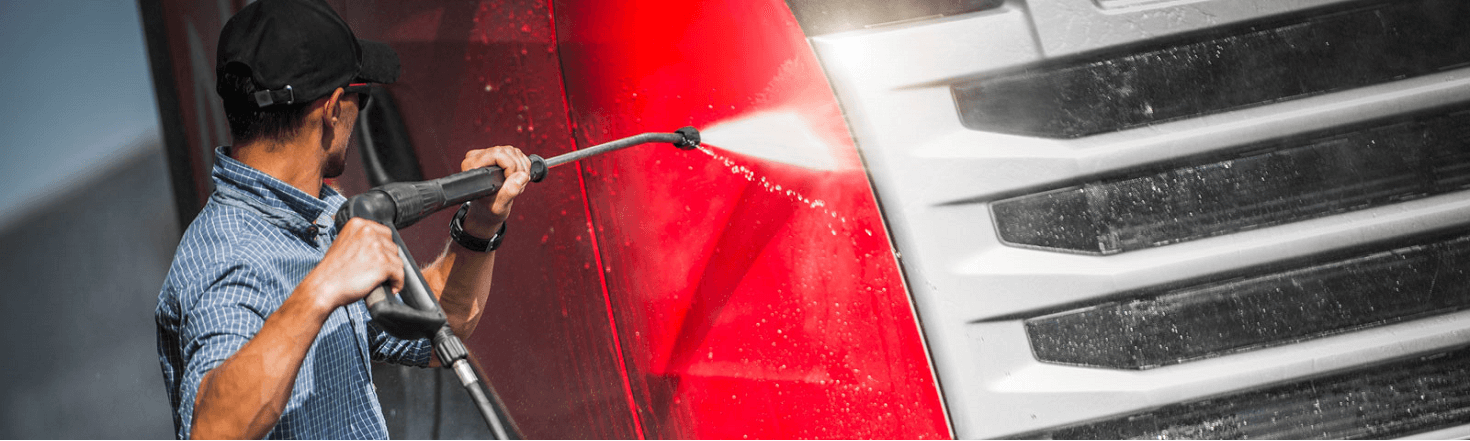 A man in plain clothes pressure washing a red semi truck.
